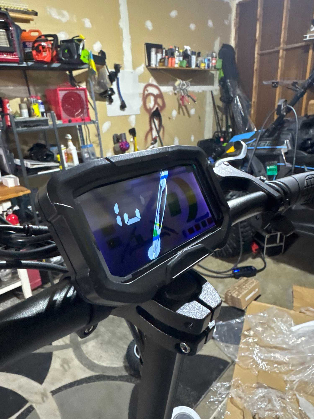 Close-up of the digital dashboard on a GlideZone GD83 electric scooter handlebar, showing the screen interface in a workshop setup for a replacement tutorial.
