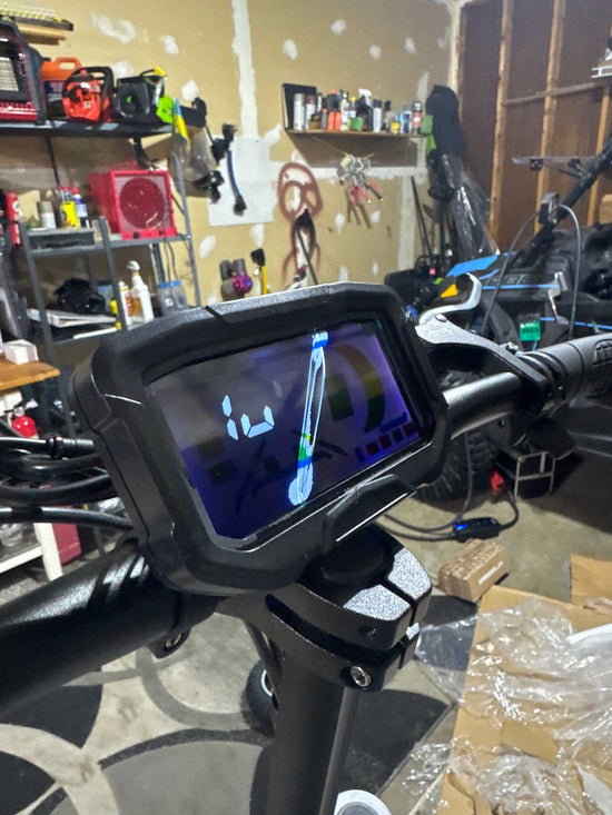 Close-up of the digital dashboard on a GlideZone GD83 electric scooter handlebar, showing the screen interface in a workshop setup for a replacement tutorial.
