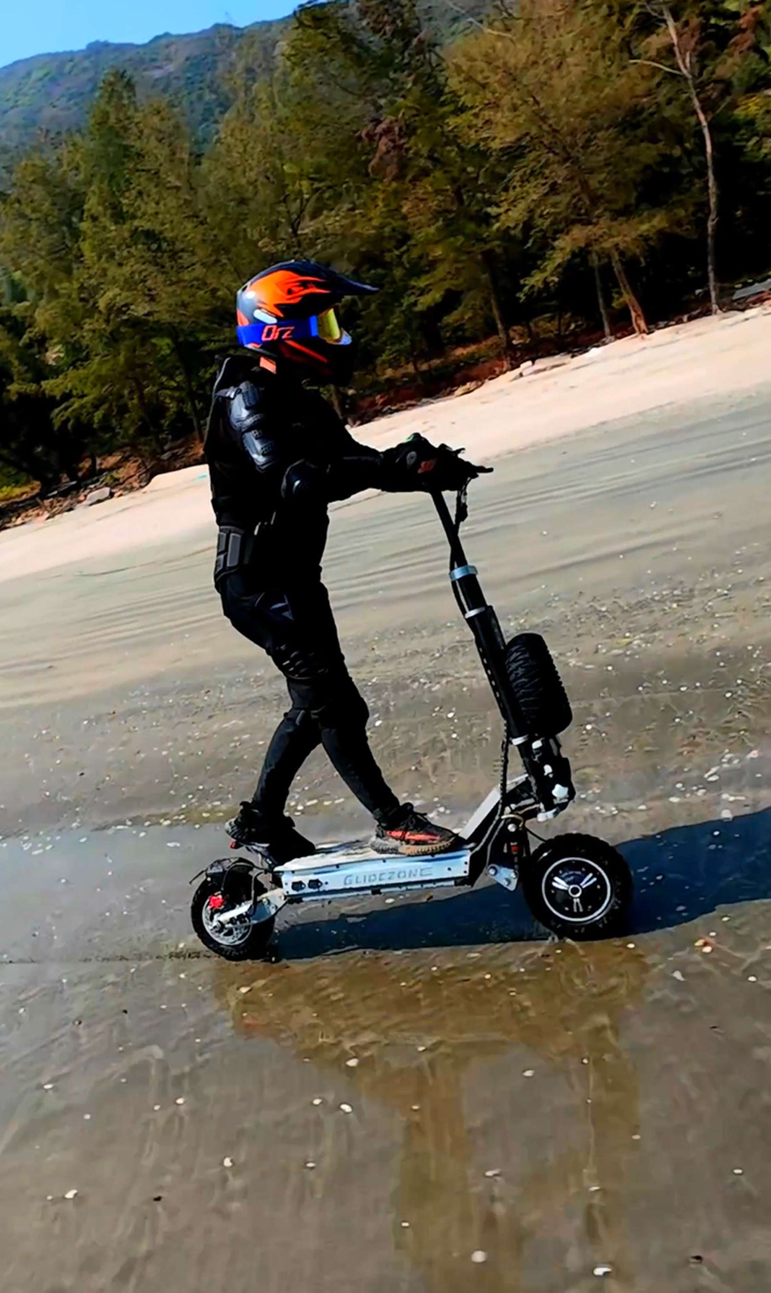 Adult rider wearing a helmet riding Glidezone GD83 through shallow water along a lake shore.