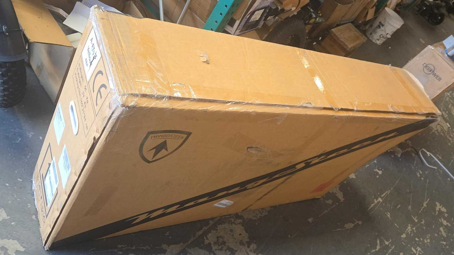 A large Mangosteen branded cardboard shipping box wrapped in clear plastic inside a US warehouse, showcasing wholesale used electric scooter or e-bike inventory ready for freight delivery.